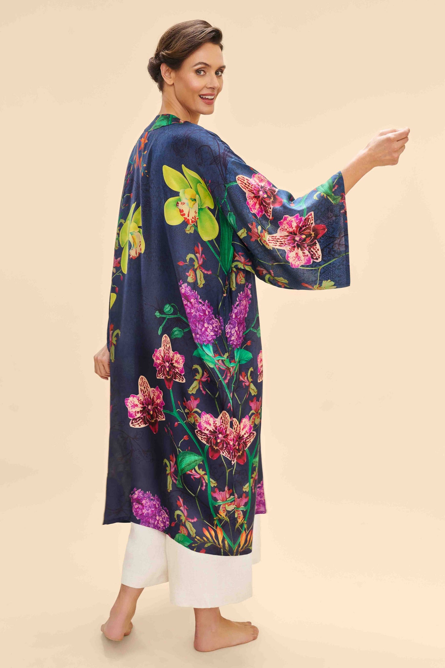 A woman standing and modeling a floral kimono gown with a dark base and vibrant flowers.